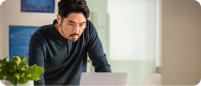 Un bărbat cu mustață și ochelari care se uită la un laptop.