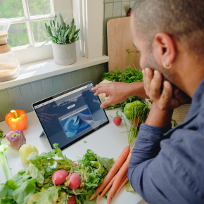 A person is seated at a kitchen counter, looking at a tablet screen displaying Microsoft Edge.