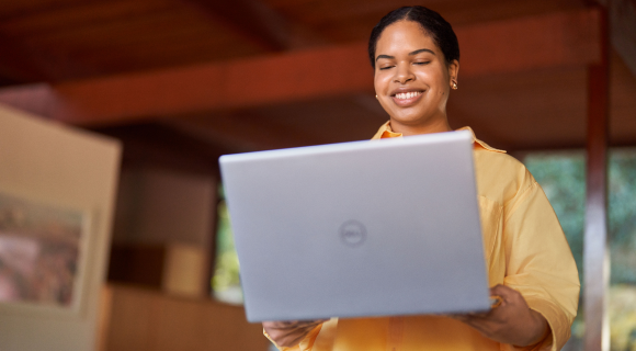 A young woman standing in a room with a laptop smiling