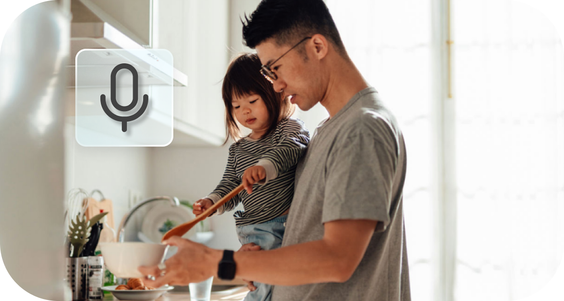 A father holds his child as they make a meal together in the kitchen.