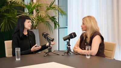 Two people speaking into microphones at a table during a recorded discussion.