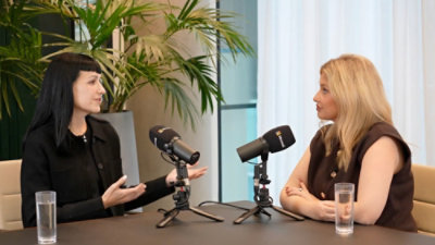 Two women siting around table with microphones