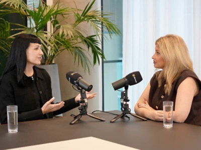 Two women siting around table with microphones.