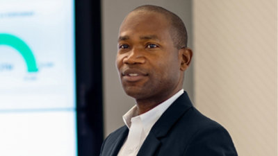 A man in a suit stands against a blue background.