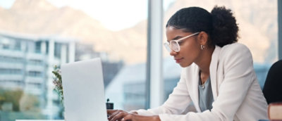 A person wearing glasses and a white jacket working on a laptop.