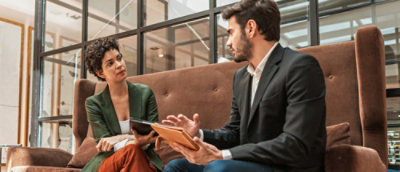 A man and a woman are seated on a couch, engaged in discussion.