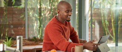 A man wearing orange sweater looking at a laptop.