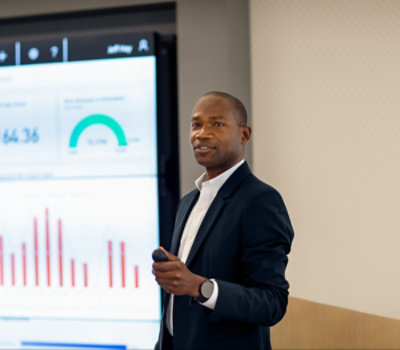 A person in a suit standing in front of a screen.