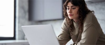 A person with long curly hair is using a laptop while seated at a table in a room with a marble wall.