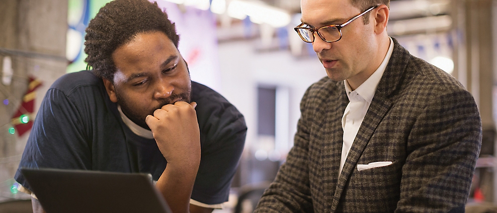 Deux hommes, un afro-américain et un blanc, qui examinent attentivement du contenu sur un ordinateur portable dans un bureau.