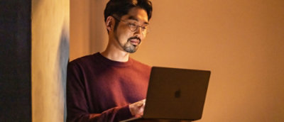 一位穿着红衬衣的男士正在使用笔记本电脑。