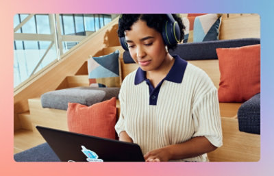 Person wearing headphones working on a laptop while seated on indoor steps.