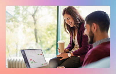 Two coworkers reviewing charts on a laptop while talking in a casual office setting.