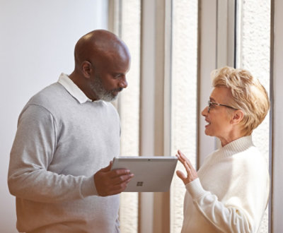 A man holding a surface pro talking to a woman