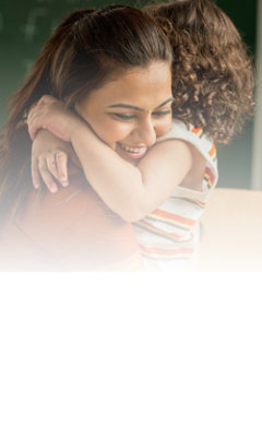 A woman smiles warmly as she lovingly hugs a child in her arms.