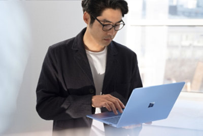 Person standing indoors using a laptop in a bright office setting.