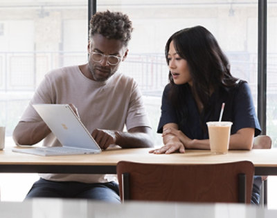 Two people sitting at a table reviewing content on a tablet, with a coffee cup nearby.