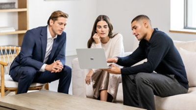 Three people reviewing content together on a laptop in a living room setting.