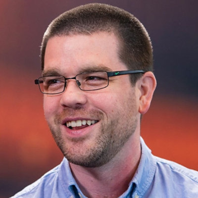 Portrait of a person wearing glasses and a blue shirt against a blurred background.