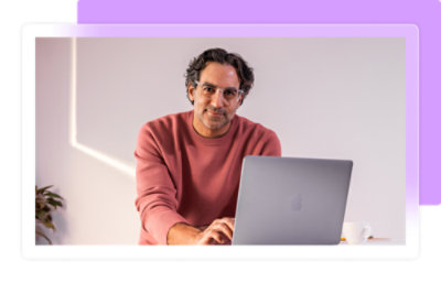 A man wearing glasses and a pink shirt sitting in front of a laptop.