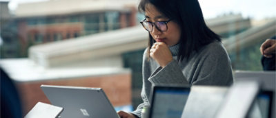 A woman with glasses and her hand on her chin staring at a laptop.