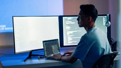 Person working at a desk with multiple monitors displaying code.
