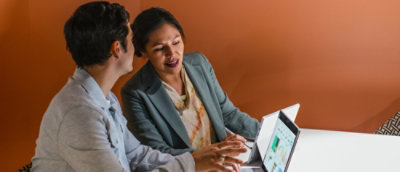 Two people sitting at a table working on laptops with charts on the screen.