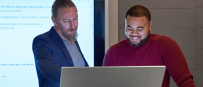 Two coworkers reviewing content together on a laptop in a meeting room.
