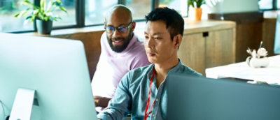 Two coworkers working together at a desktop computer in a modern office.