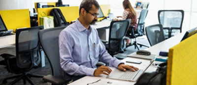A man wearing glasses looking at the laptop screen in the office environment