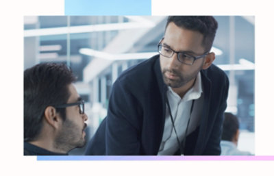 Person in a dark jacket leaning over to speak with another person in a modern office setting.