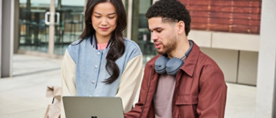 A man wearing headphones around his neck and a woman looking at a laptop.