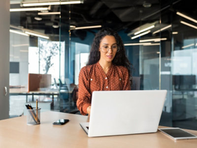 Woman with curly hair in brown shirt looking at a laptop and working