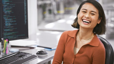 A woman smiling and looking at a computer screen.
