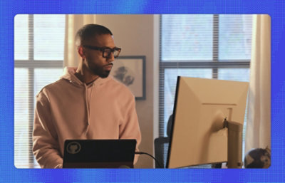A man in a pink sweatshirt looking at a computer monitor.