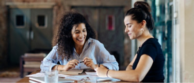 Two individuals sitting at a table with papers and a glass of water, engaged in a discussion.