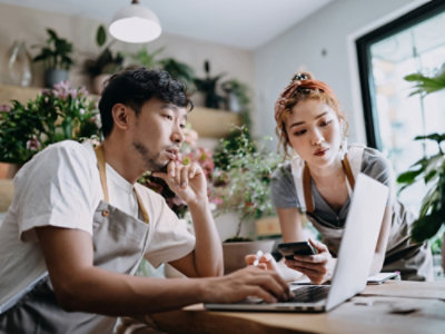 Two people sitting, looking at a laptop and having a discussion.