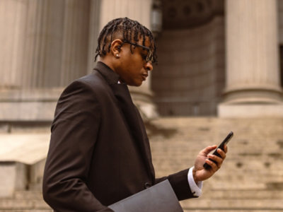 A working professional holding a laptop and looking at the mobile phone