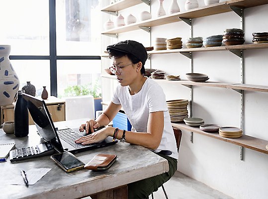 A woman at a pottery shop, using a laptop computer to work
