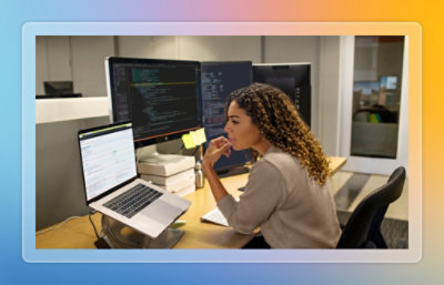 Person working at a desk with laptop and multiple monitors displaying code and dashboards.