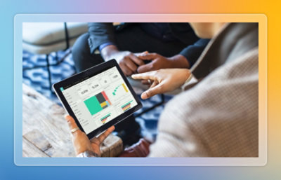 Hands holding a tablet displaying dashboards and charts during a business discussion at a table.