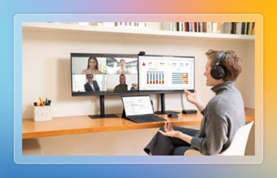 Person participating in a video call at a desk with dual monitors showing dashboards and charts.
