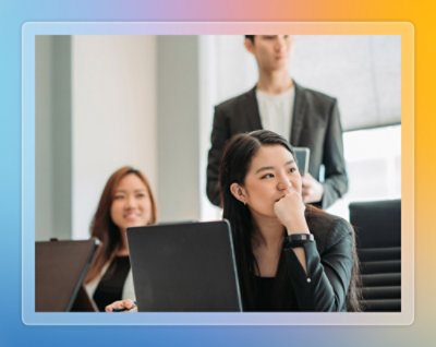Person working on a laptop while colleagues stand and sit nearby in an office.