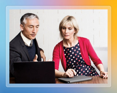 Two colleagues discussing work while seated at a table with a laptop.