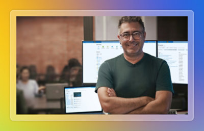 Man standing with arms crossed and smiling in front of multiple monitors