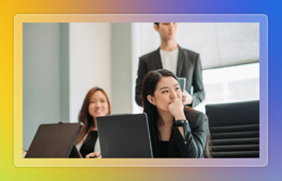 Professionals work on laptops in a meeting room while a colleague stands and observes.