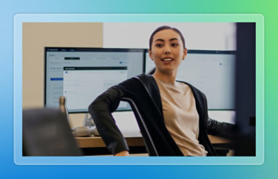 Person seated at a desk in a modern workspace, facing multiple computer monitors with a laptop and keyboard visible in the background.