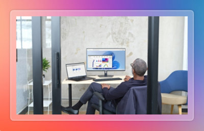 Man sitting at desk looking at desktop and laptop screen