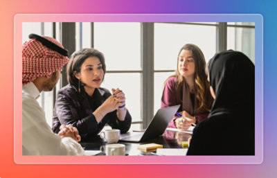 People seated around a table, having a discussion with notebooks and cups.