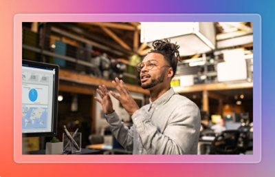 Person gesturing toward a computer monitor displaying charts in an industrial workspace.